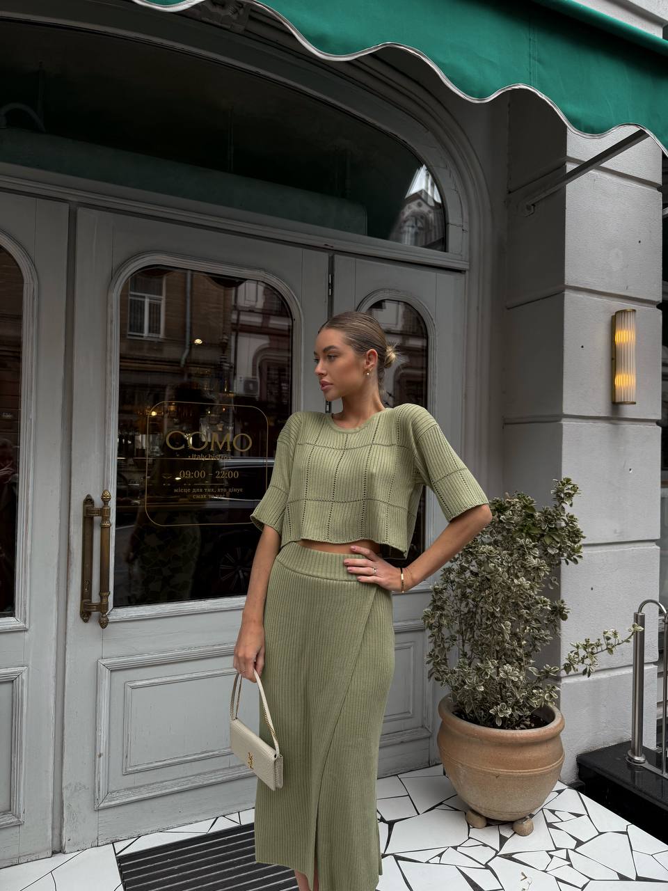 Woman in a green outfit standing in front of a building entrance.
