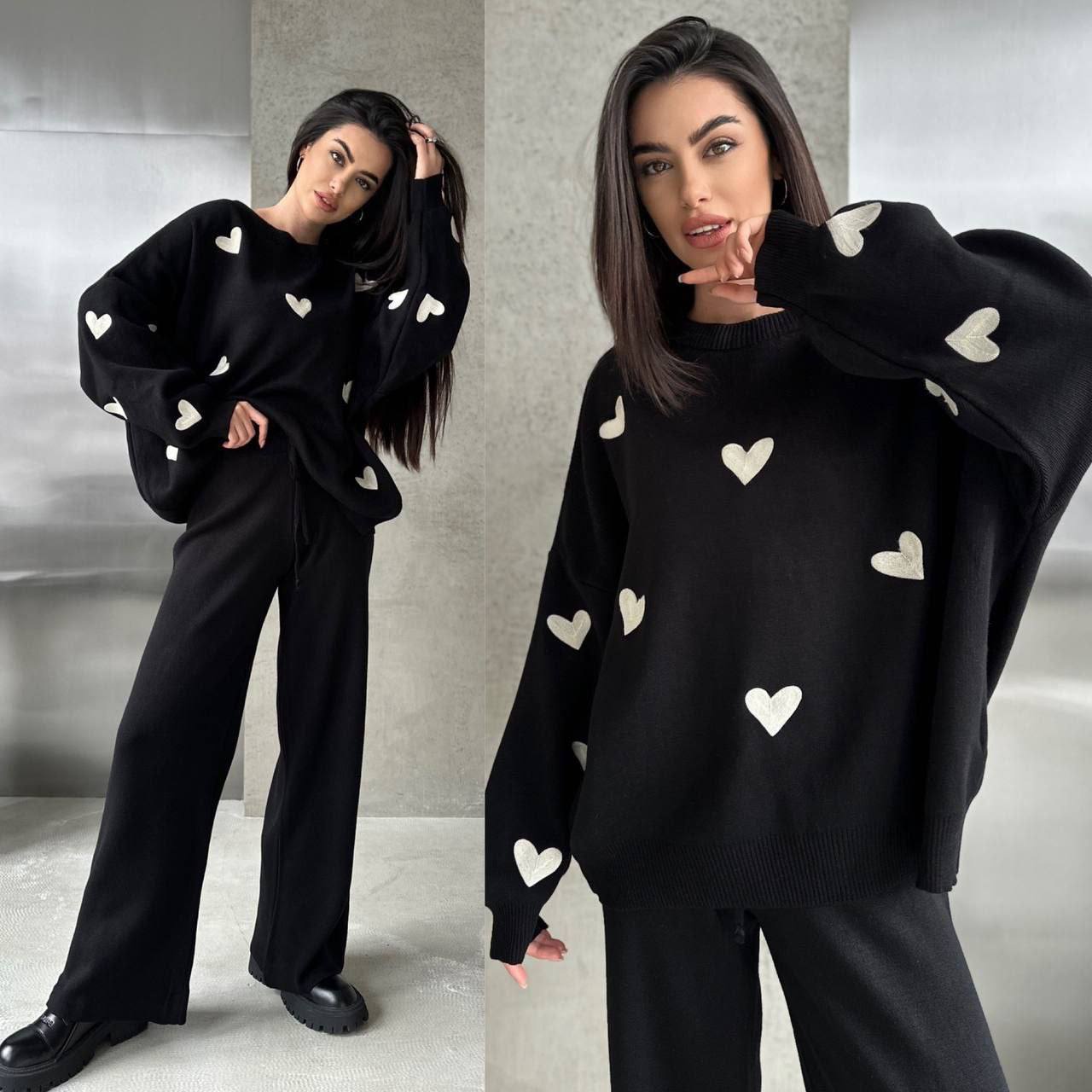 Woman wearing a black sweater with heart patterns in a minimalistic setting
