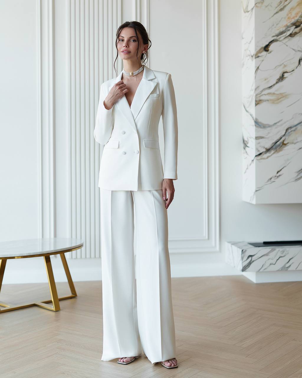 Woman wearing a white suit in a stylish room with marble wall.