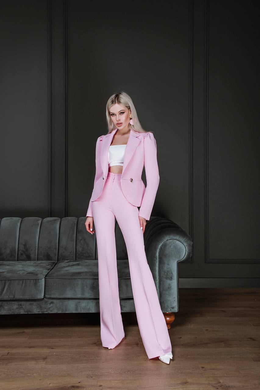 Woman in a pink suit standing in a room with a gray couch.