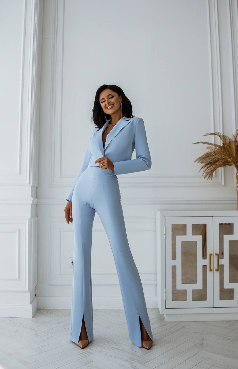 Woman wearing a light blue jumpsuit in an elegant room with white walls and decorative elements.
