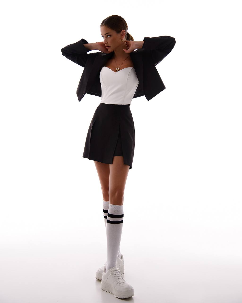 Woman wearing a black blazer, white top, black skirt, and white shoes with black stripes on a white background