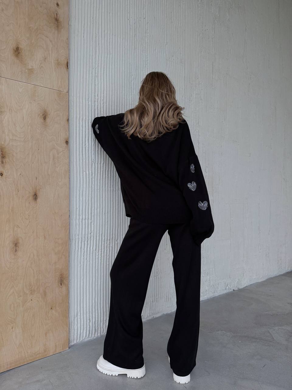 Person wearing a black outfit with heart details against a neutral wall.