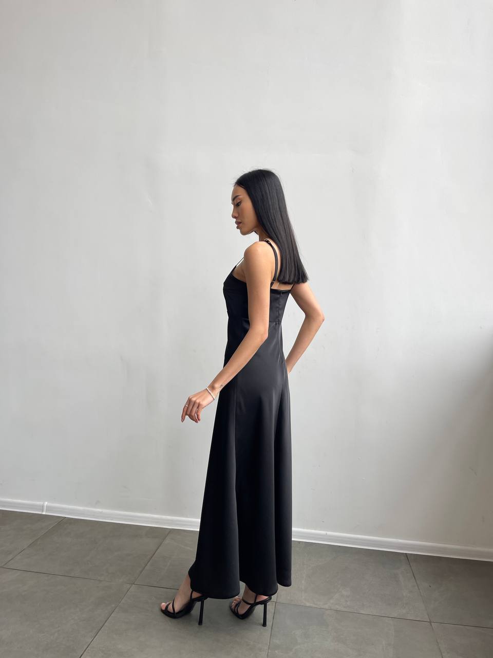 Woman wearing a black sleeveless dress against a plain white wall.