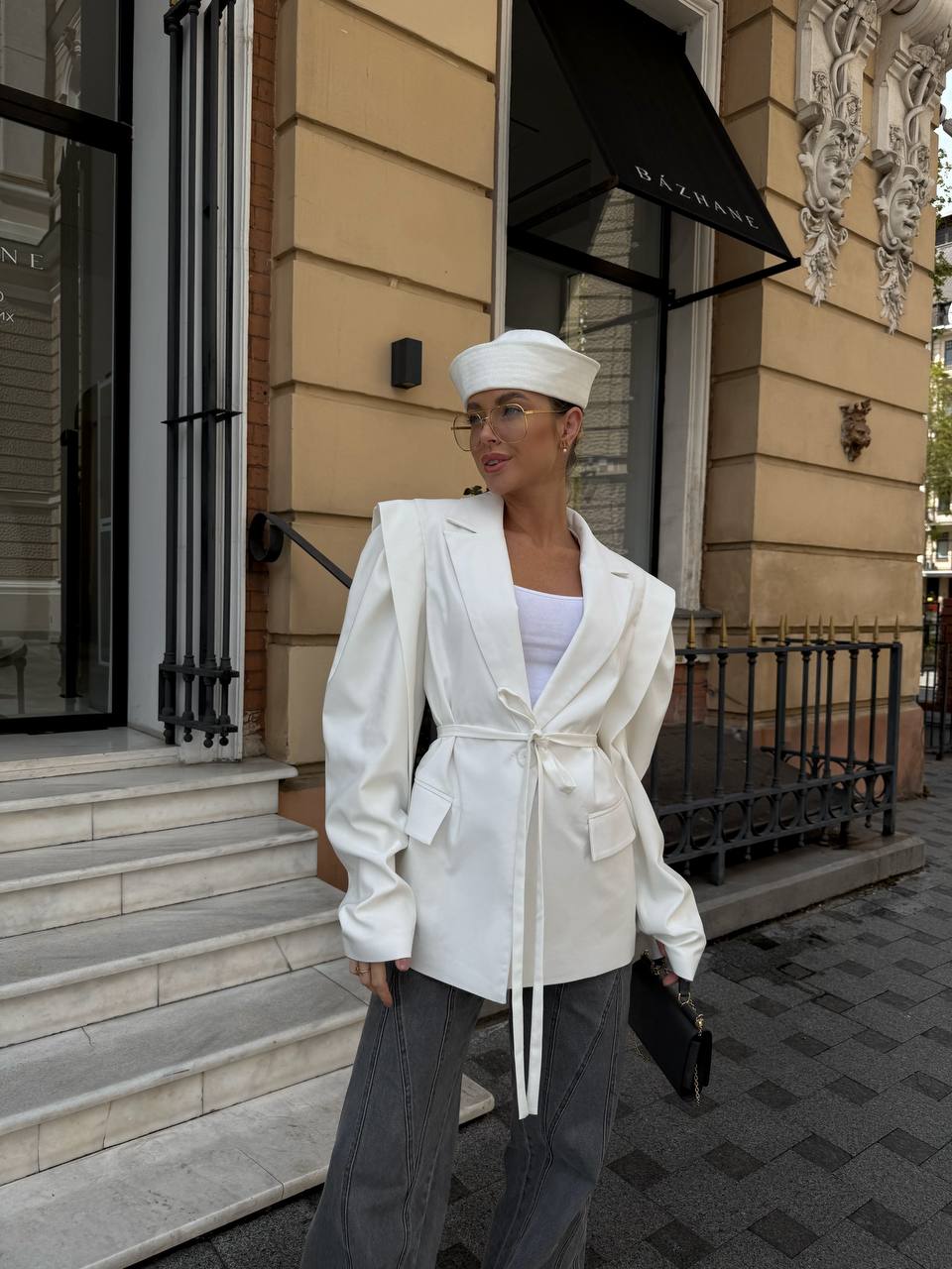 Woman in a white outfit standing in front of a building with a black awning.