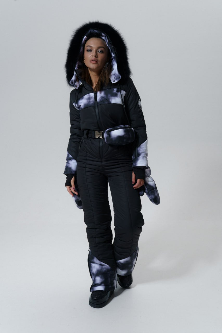 Person wearing a black and white tie-dye jacket with fur hood on a gray background