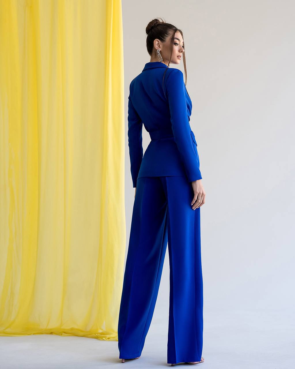 Woman in a blue outfit standing against a yellow curtain and white wall
