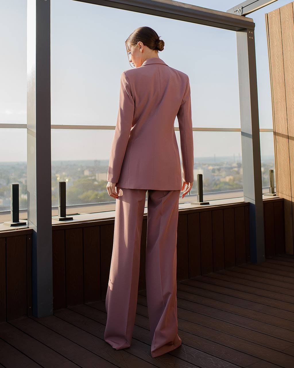 Woman in a pink suit standing on a rooftop with a cityscape view.