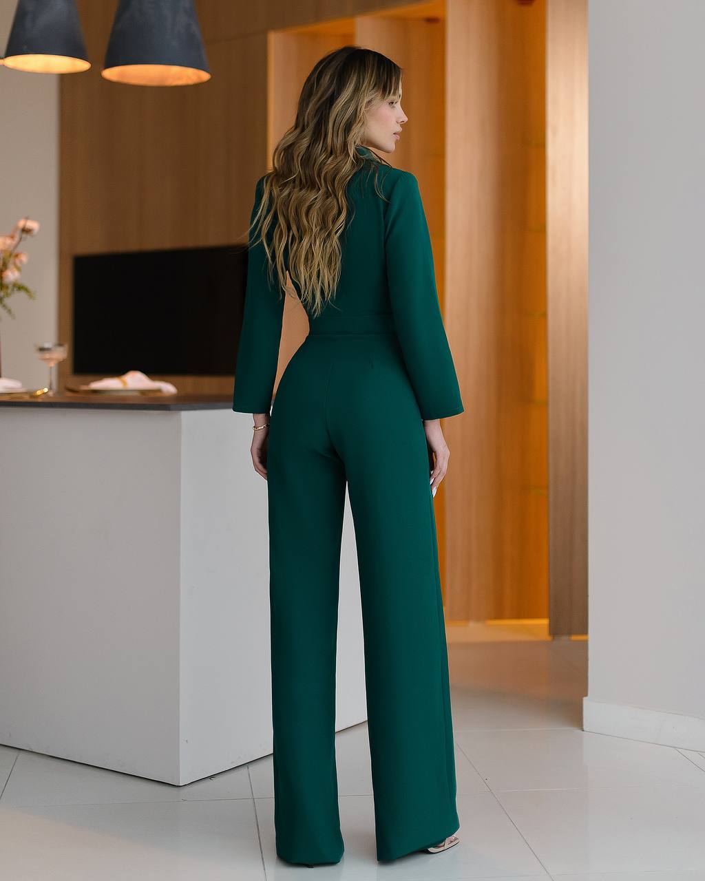 Woman in a green jumpsuit standing in a modern interior setting.