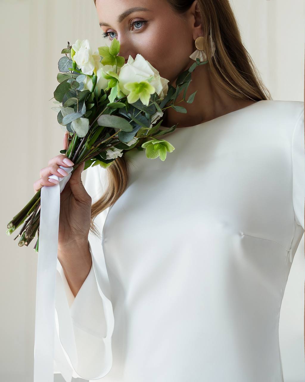 Woman in a white dress holding a bouquet of flowers against a plain background