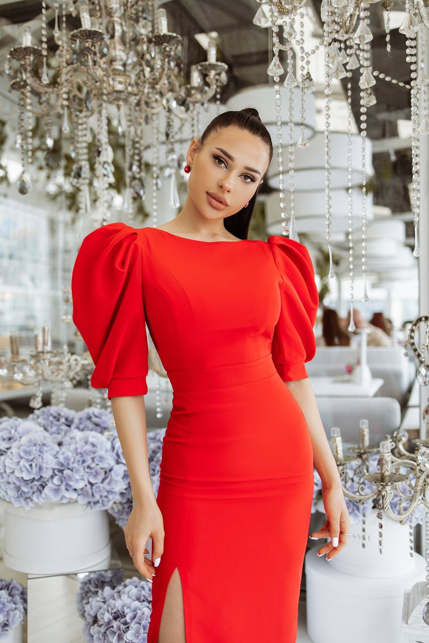Woman in a red dress standing in an elegant interior setting with chandeliers and floral arrangements.