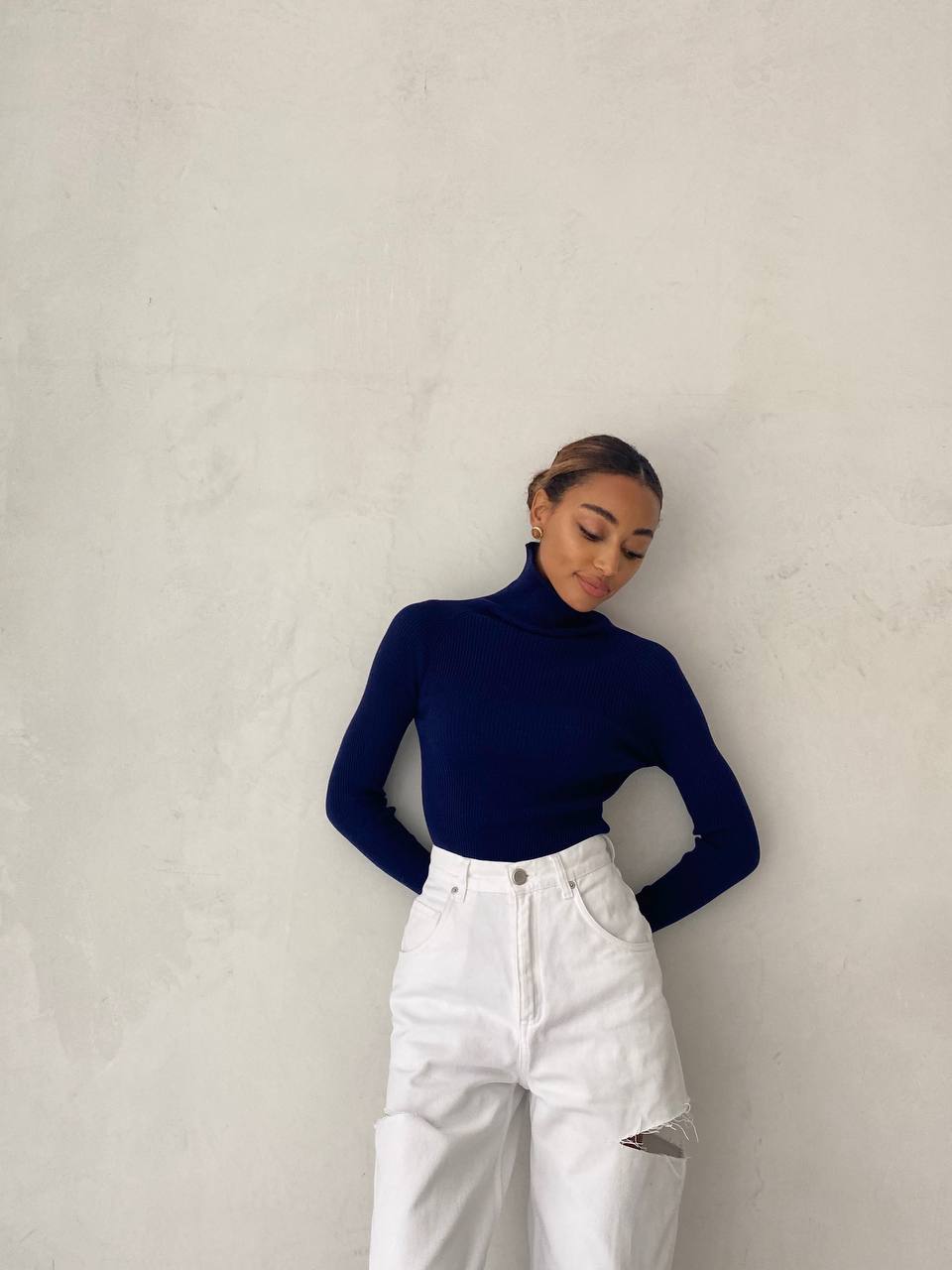 Person wearing a navy turtleneck and white pants against a plain background