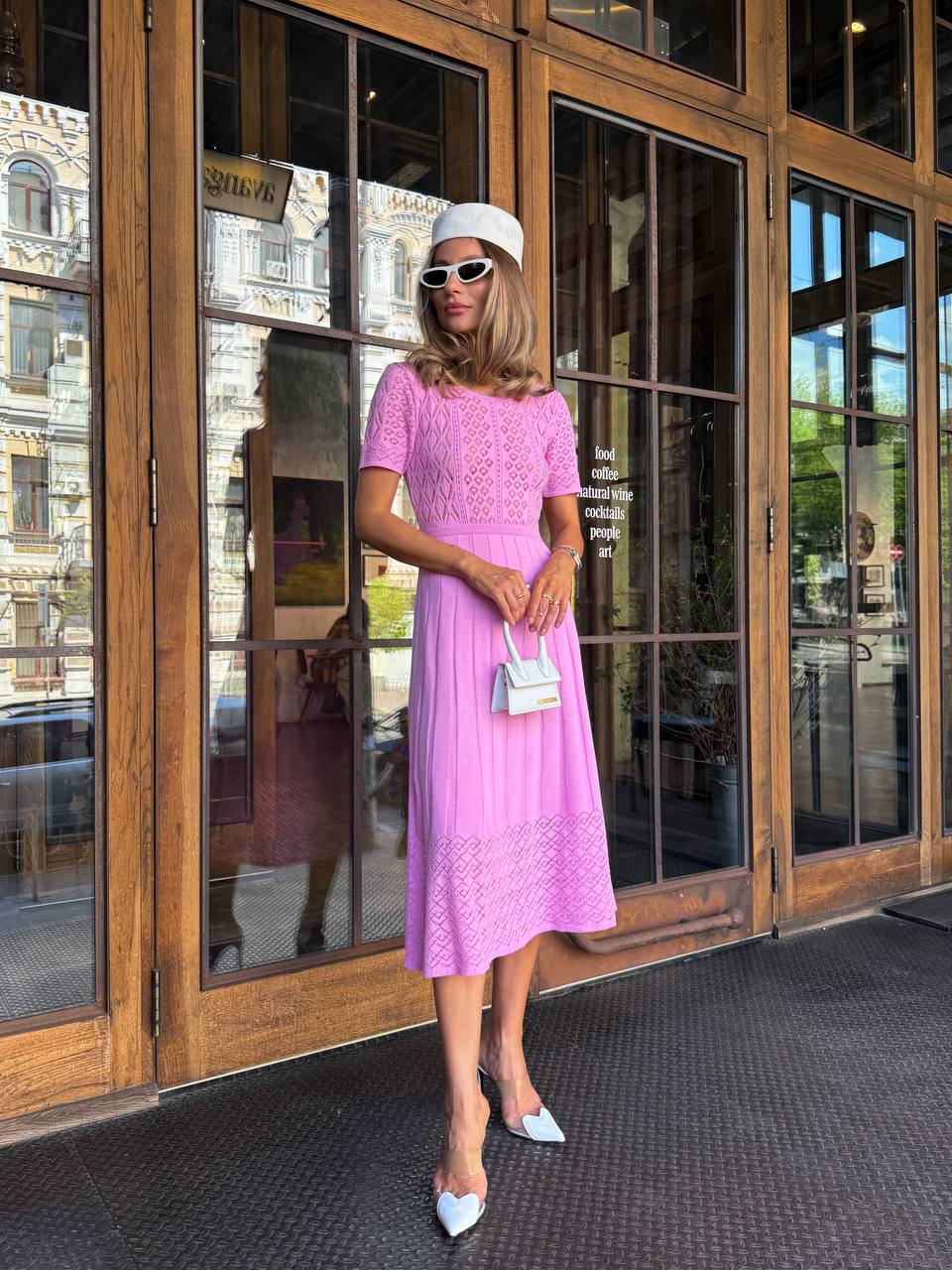 Woman in a pink dress standing in front of large glass doors.