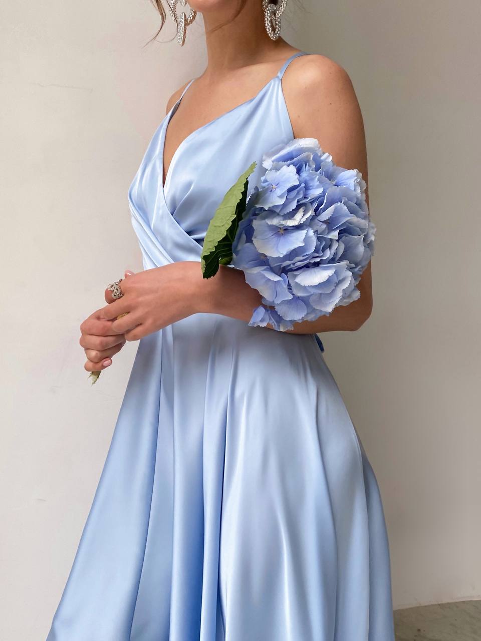 Woman in a light blue dress holding a bouquet of flowers against a plain background