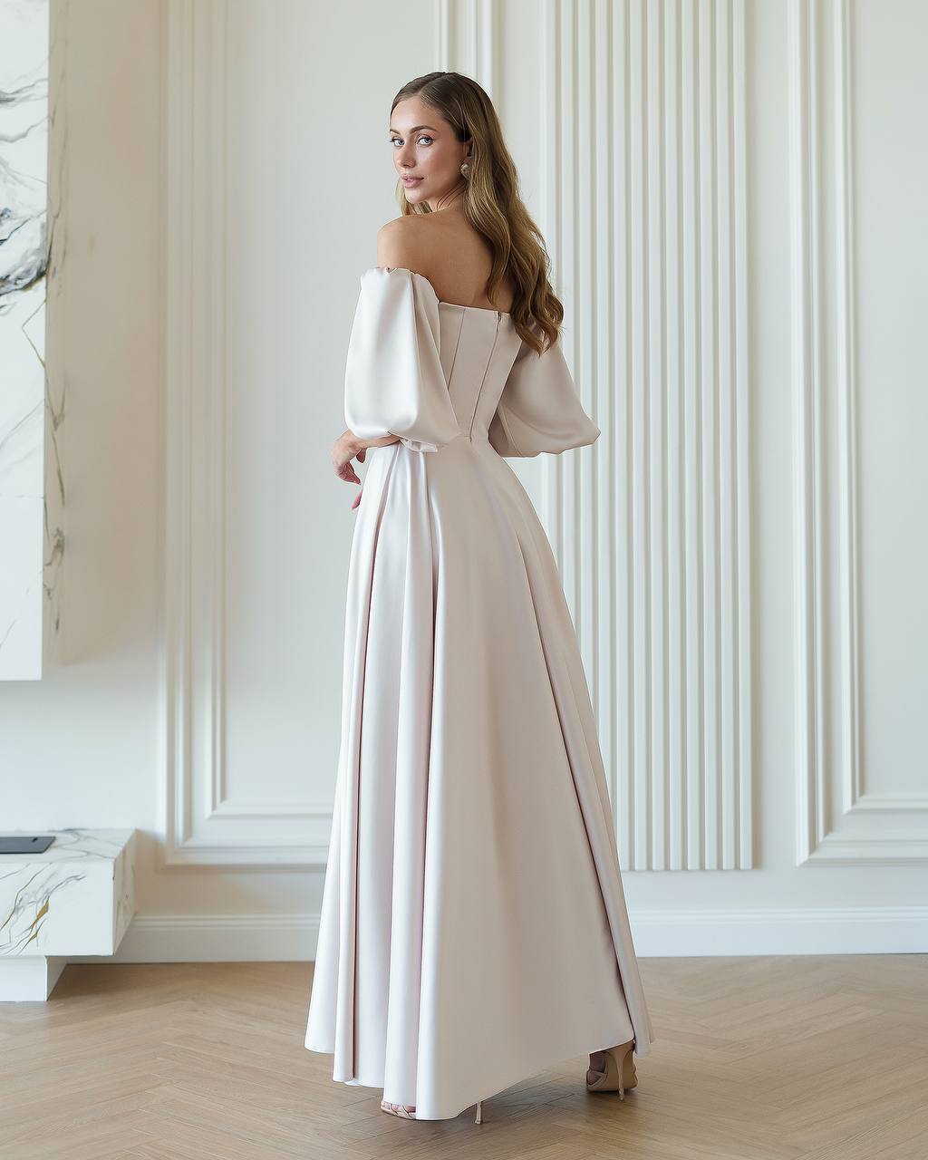 Woman wearing a long, elegant dress in a room with white walls and wooden floor.