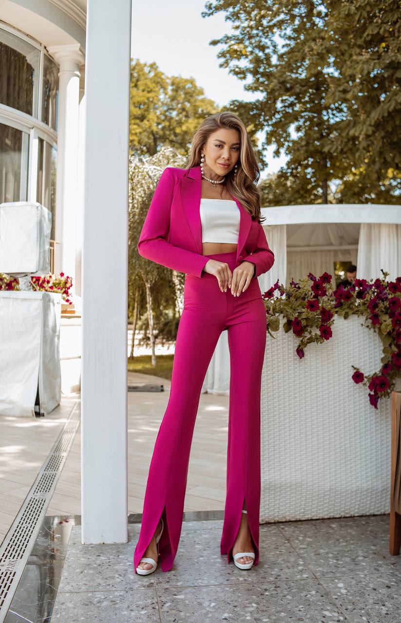 Woman in a pink outfit standing outdoors with greenery and flowers in the background