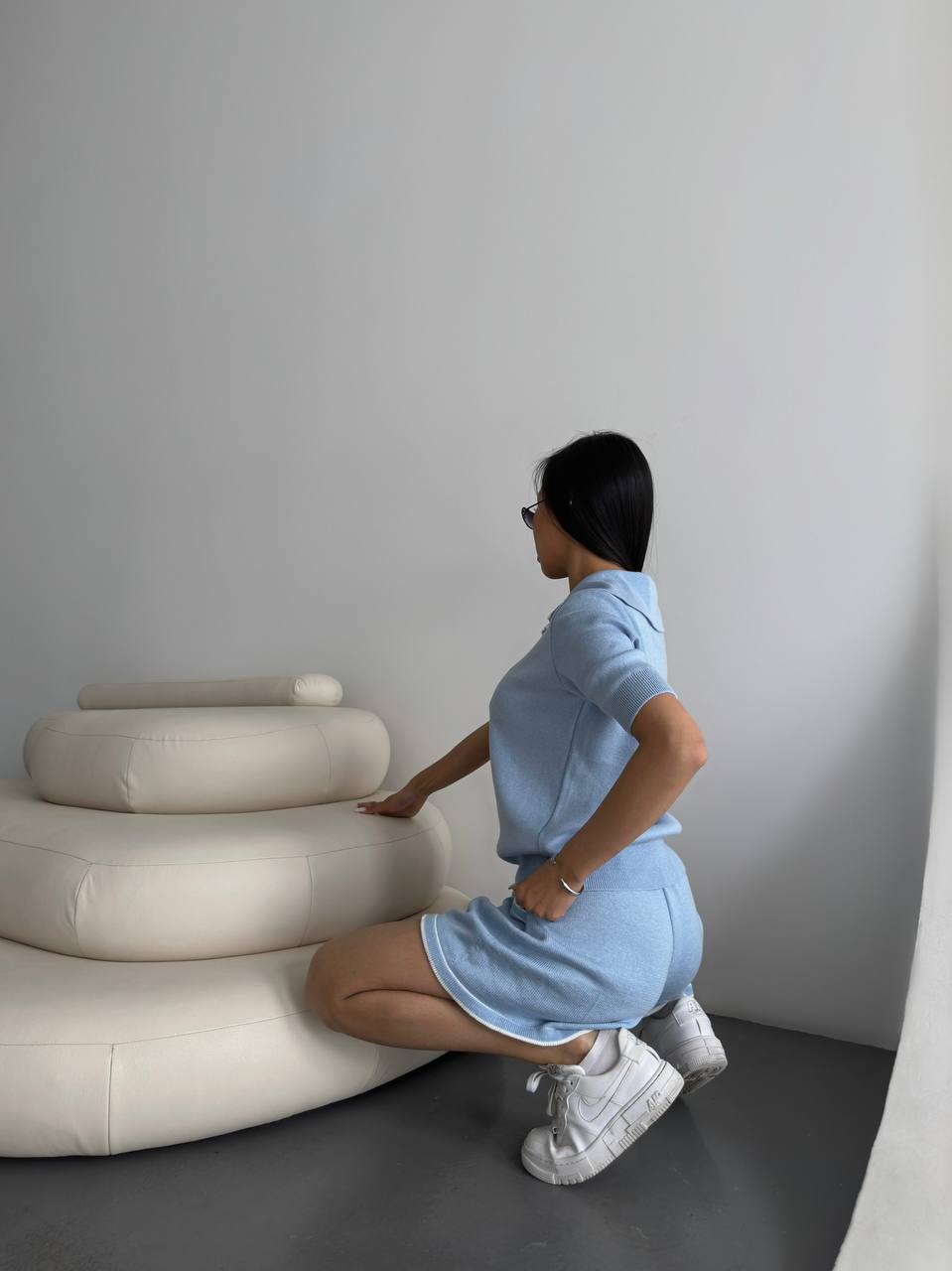 Person in a light blue outfit interacting with a modern white sculpture against a plain wall.