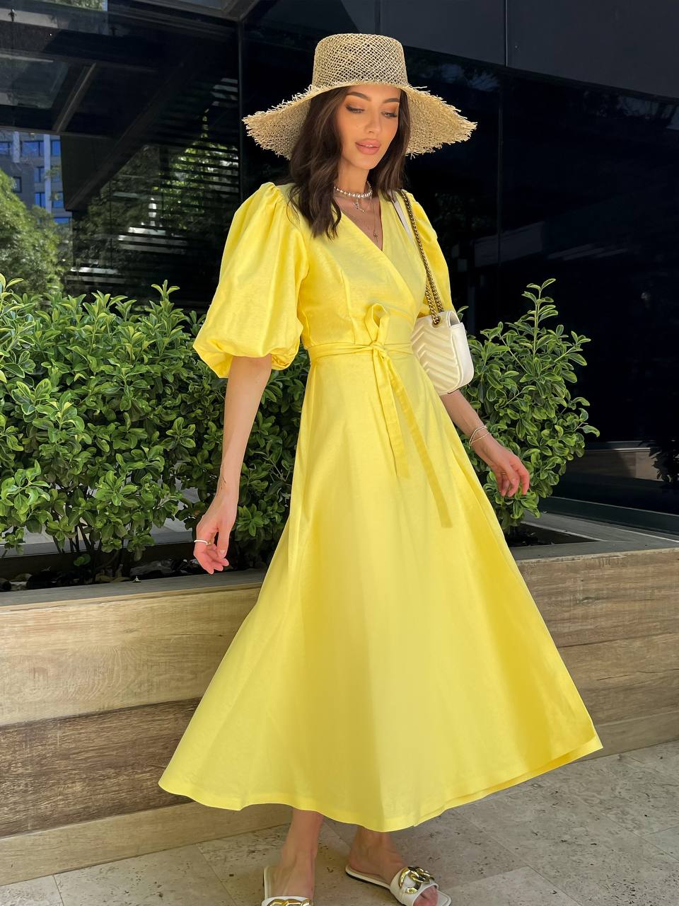 Woman in a yellow dress and straw hat standing outdoors.