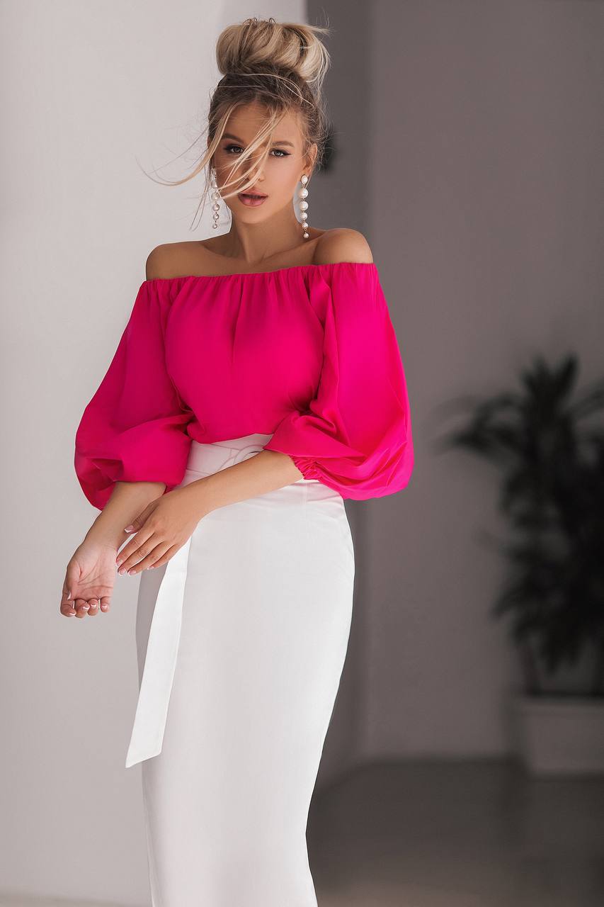Woman wearing a bright pink off-shoulder top and white pants indoors.