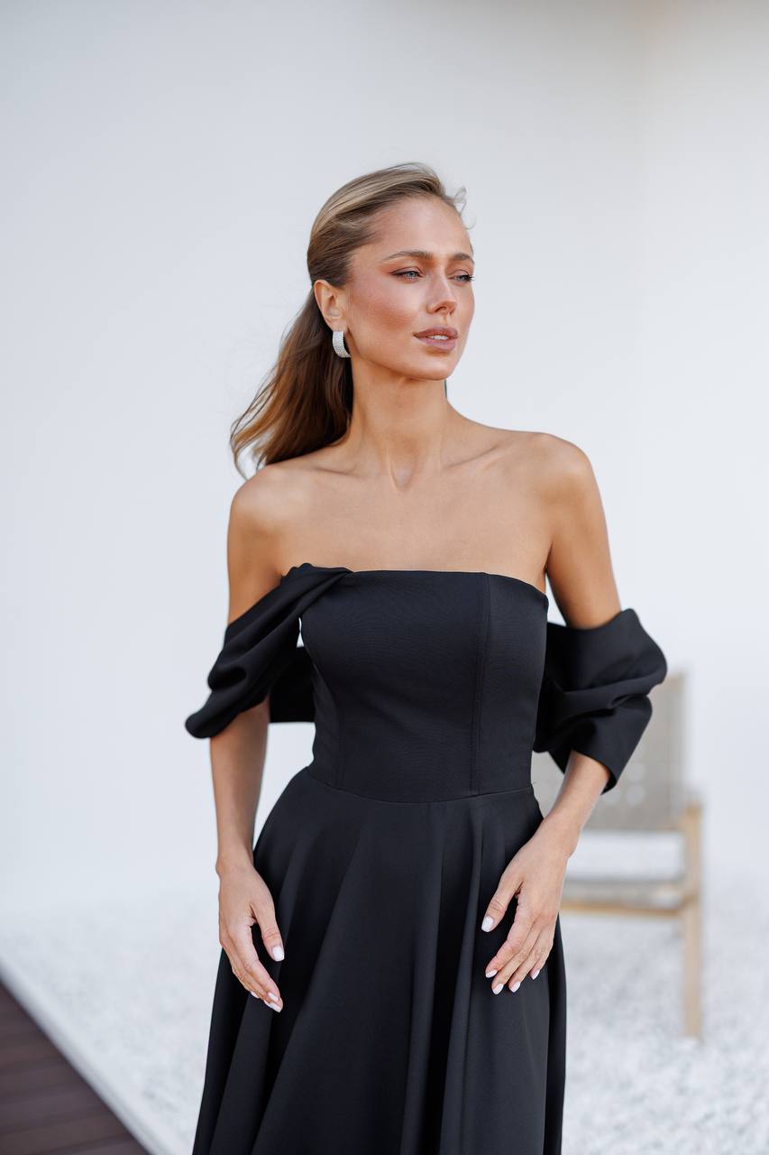 Woman wearing a black off-shoulder dress with puffed sleeves against a white background