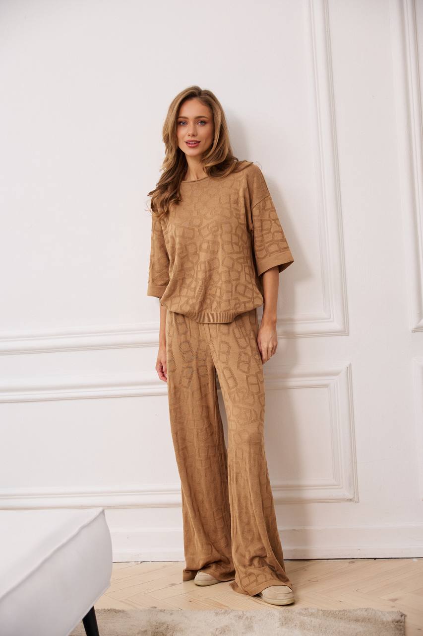Woman wearing a brown outfit standing against a white wall.