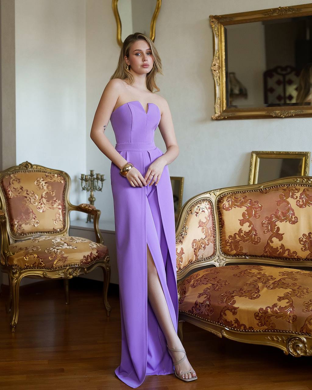 Woman in a purple strapless gown standing in an ornate room with gold accents.