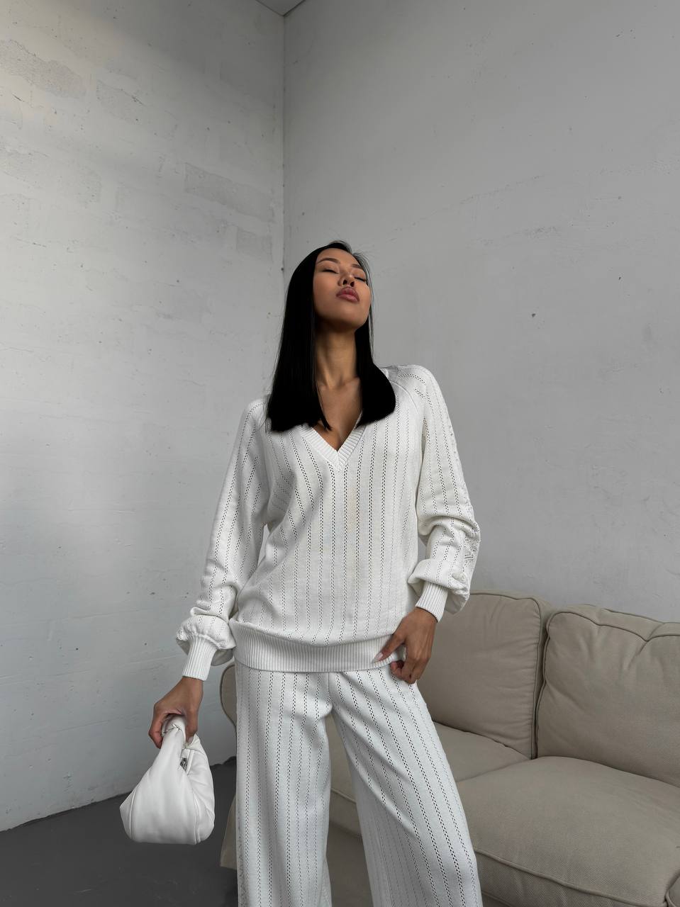Woman in a white outfit standing in a minimalistic room with a beige couch.