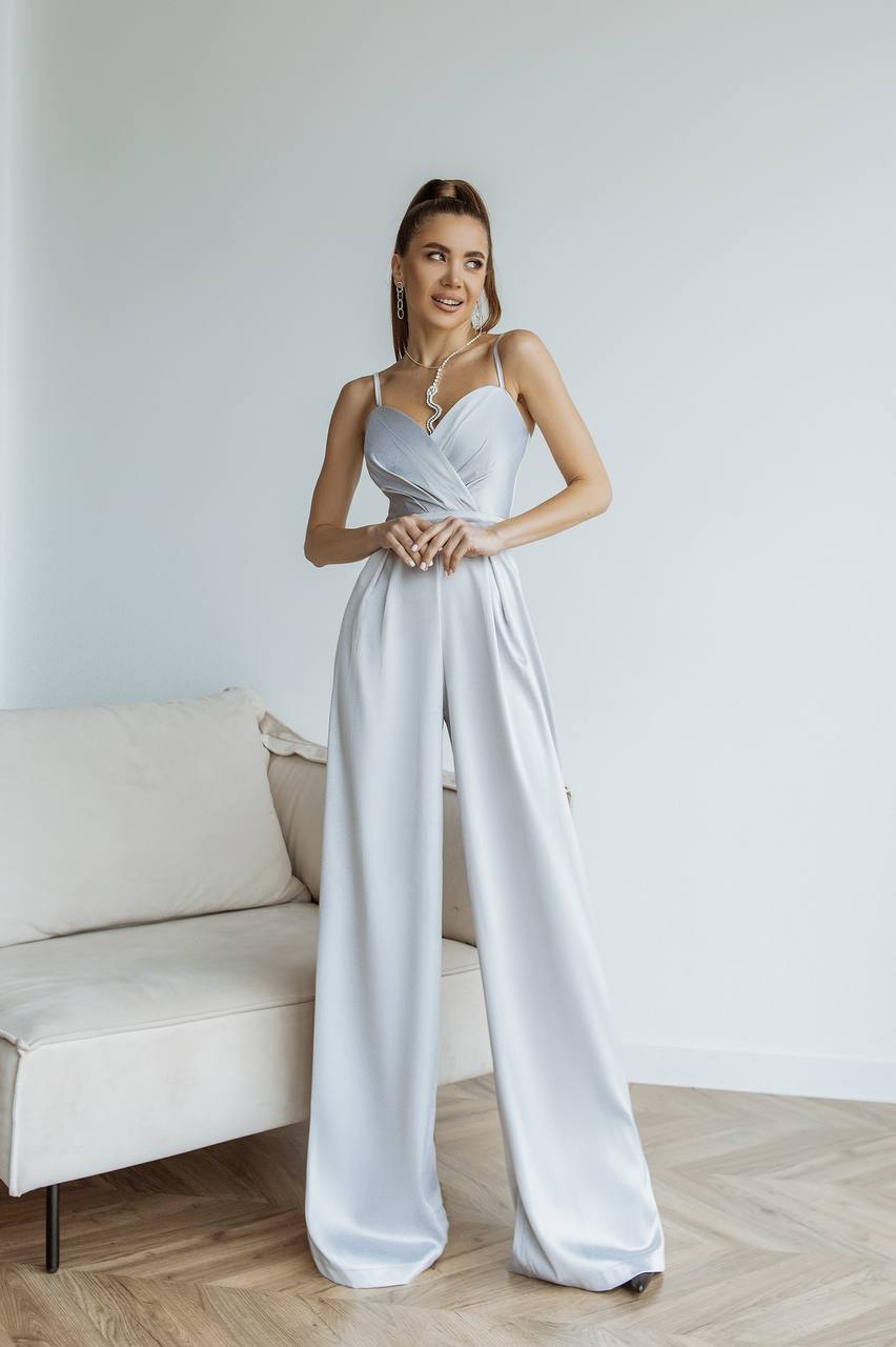 Woman wearing a light gray jumpsuit standing in a minimalistic room with a white couch.
