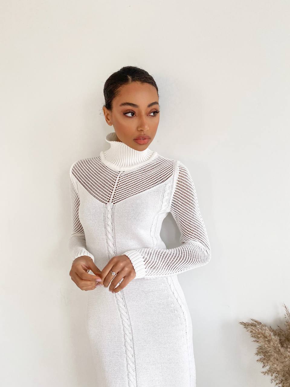Woman wearing a white turtleneck sweater with a textured pattern against a plain background