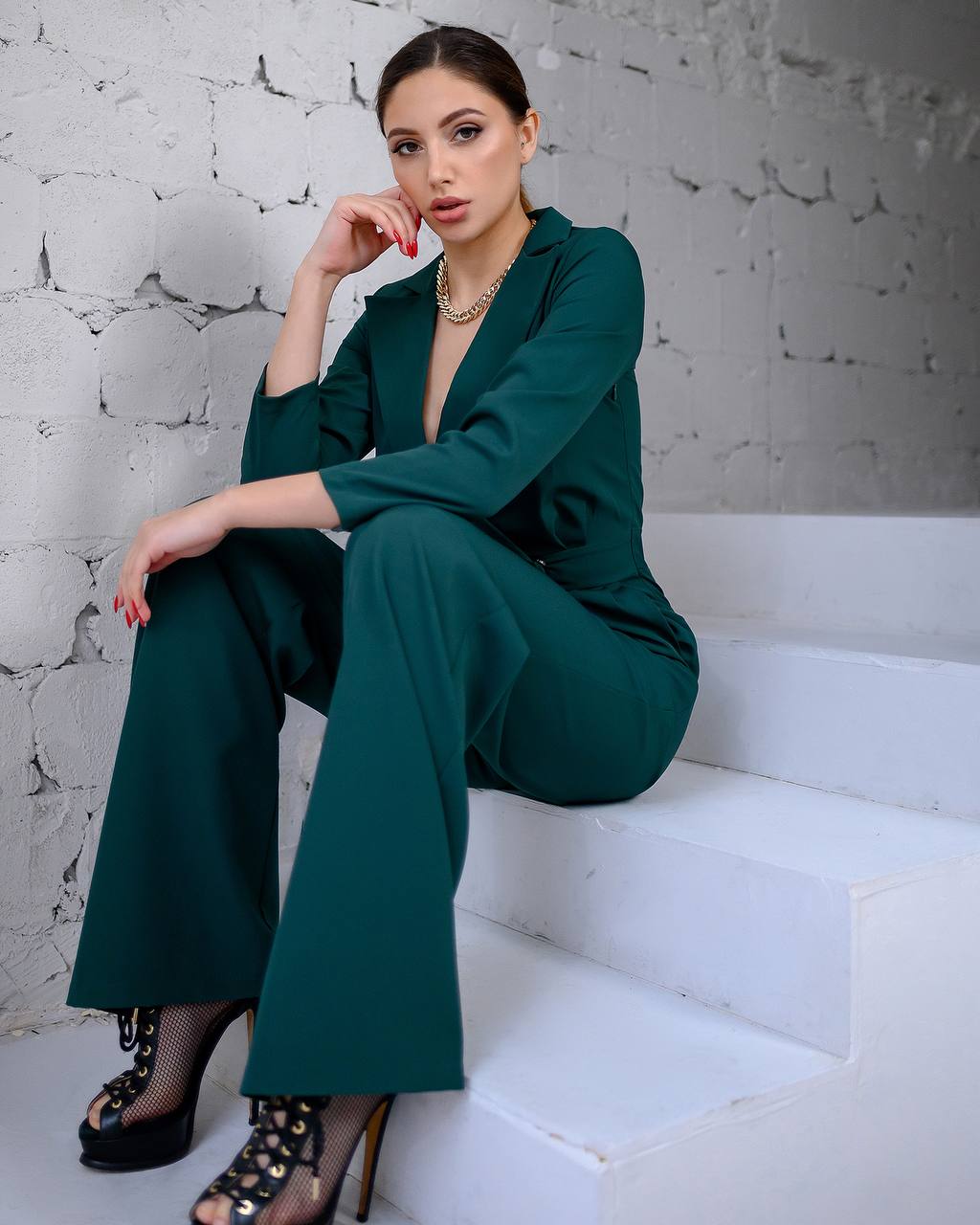Woman in a green outfit sitting on white steps with a textured white wall background