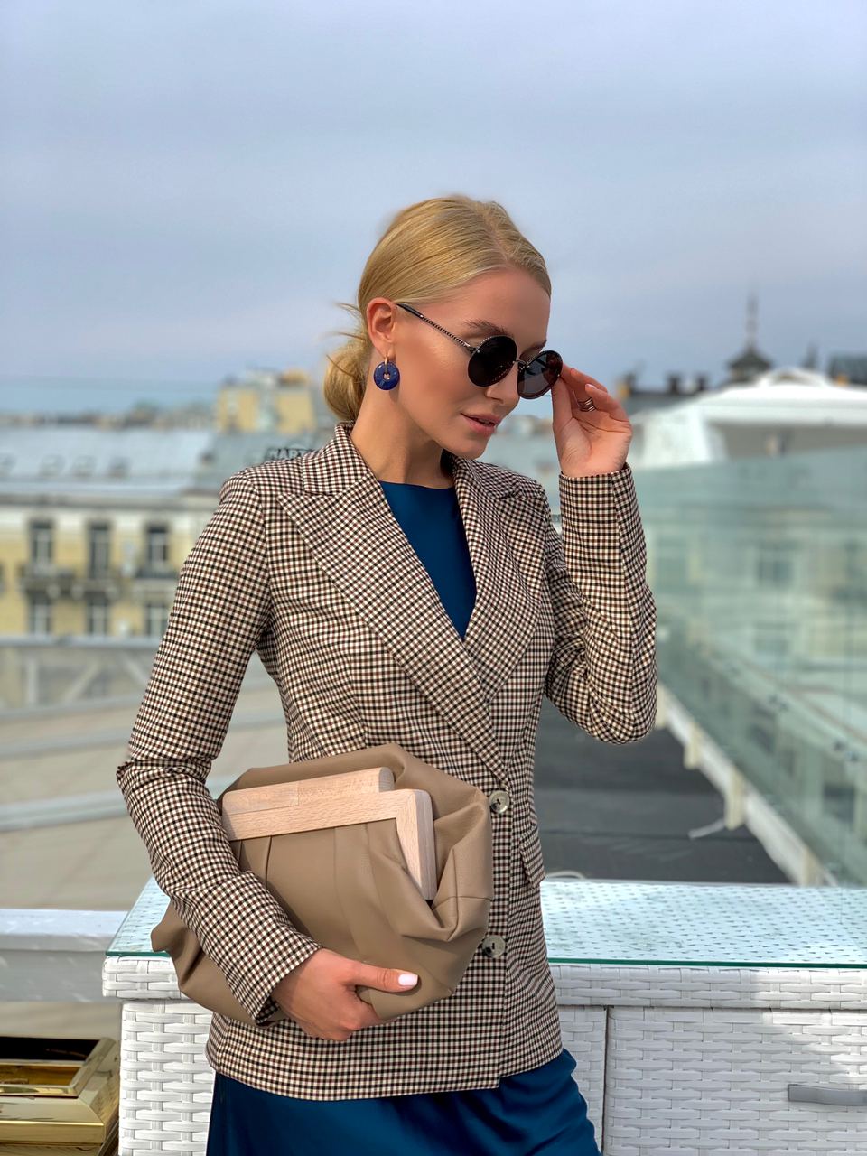 Woman in a checkered blazer holding a beige clutch with a cityscape background