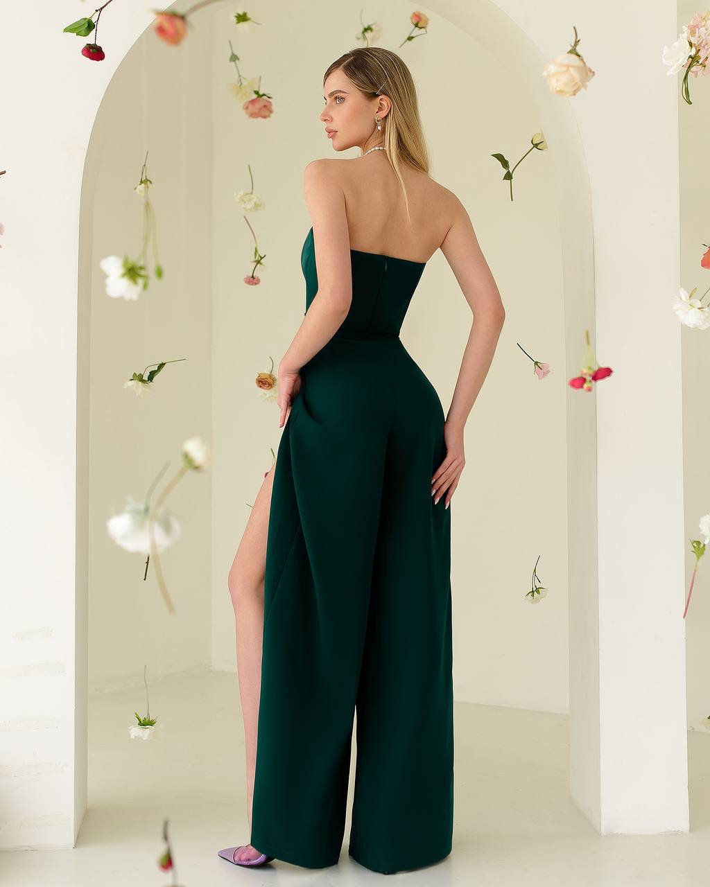 Woman wearing a dark green strapless jumpsuit with floral decorations on a light background