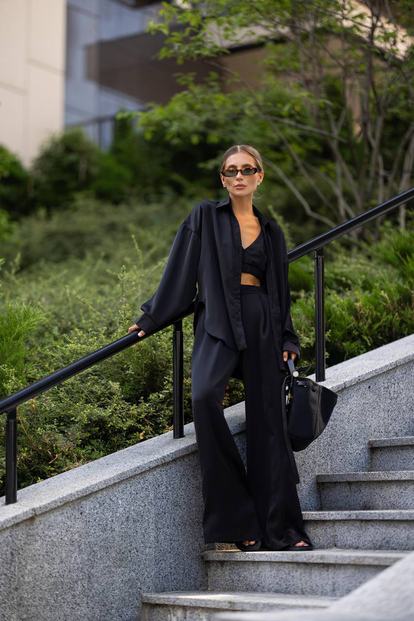 Woman in black outfit standing on outdoor steps with greenery in the background