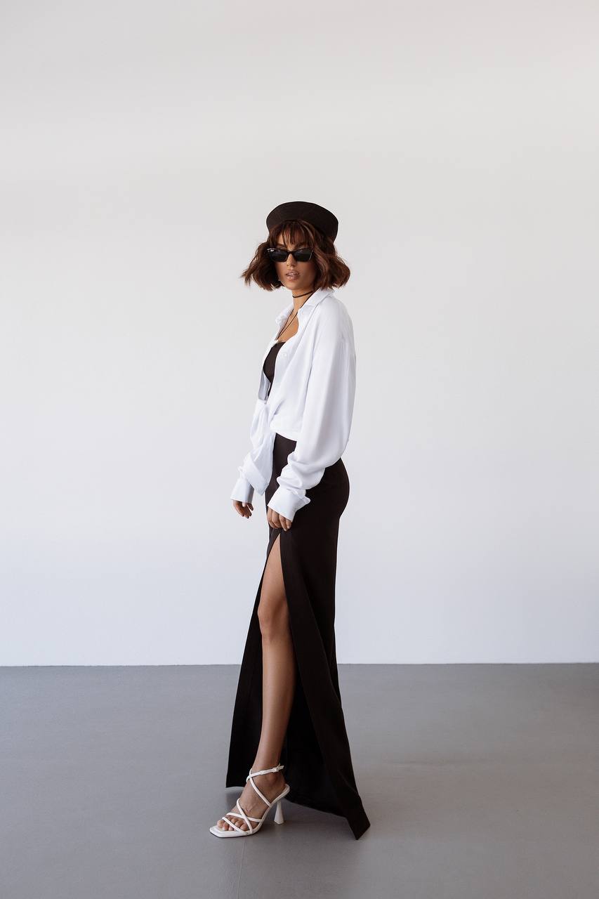 Woman wearing a white shirt, black skirt, and hat against a plain background