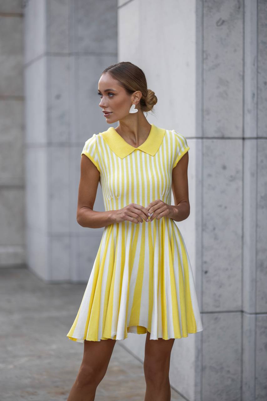 Woman wearing a yellow and white striped dress standing against a gray stone wall.