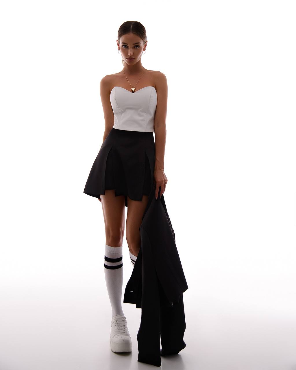 Woman wearing a white strapless top and black skirt with a black jacket over her shoulder on a white background