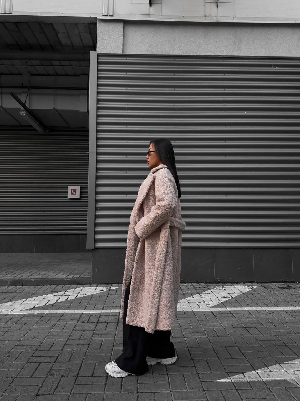 Person wearing a long coat standing on a street with a building in the background