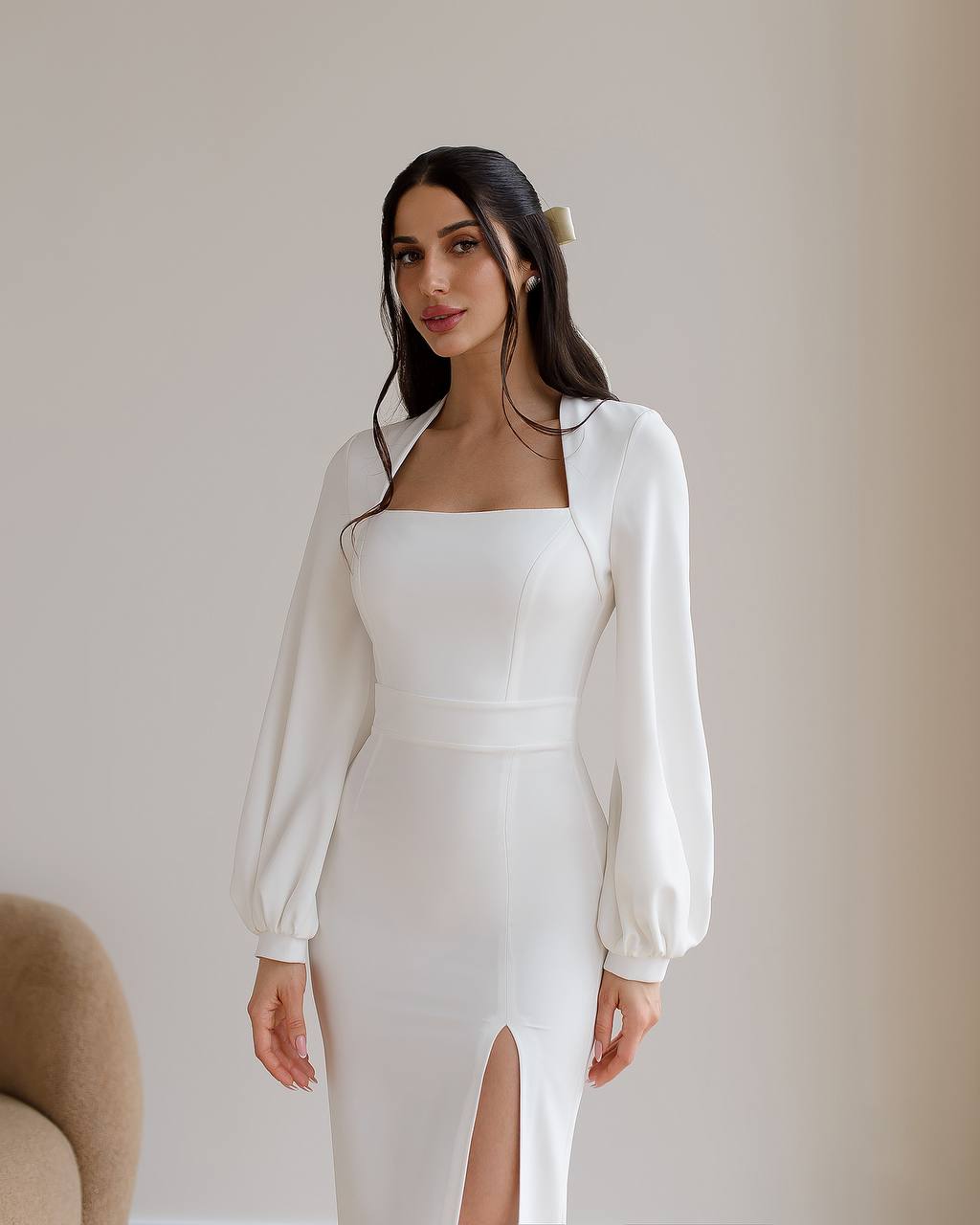 Woman wearing a white dress with long sleeves against a plain background