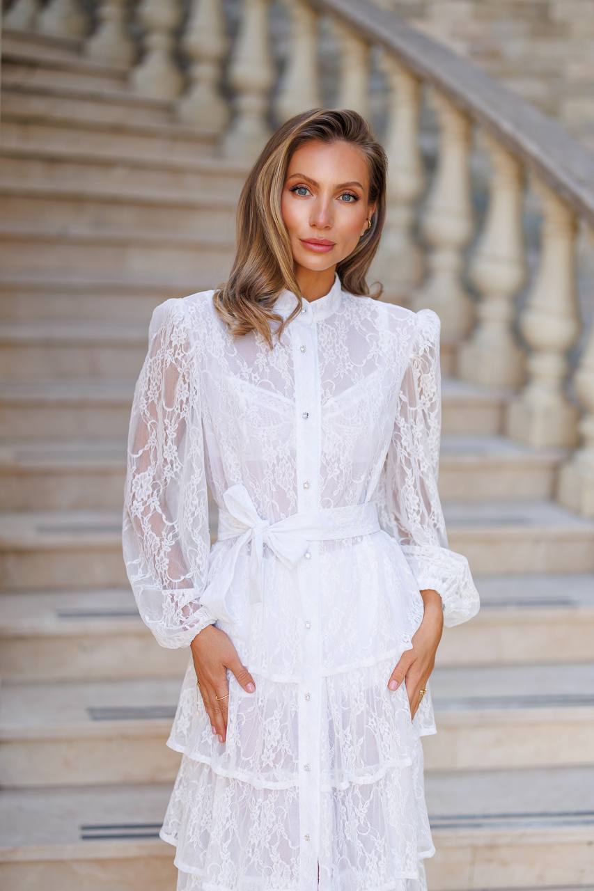 Woman in a white lace dress standing on stone steps.