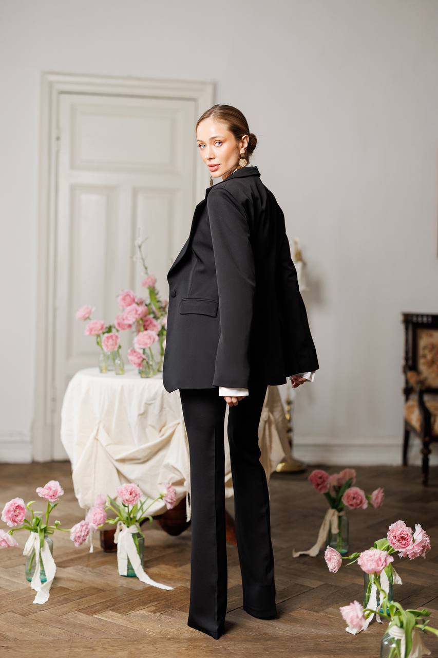Woman in a black suit standing in a room with floral decorations.