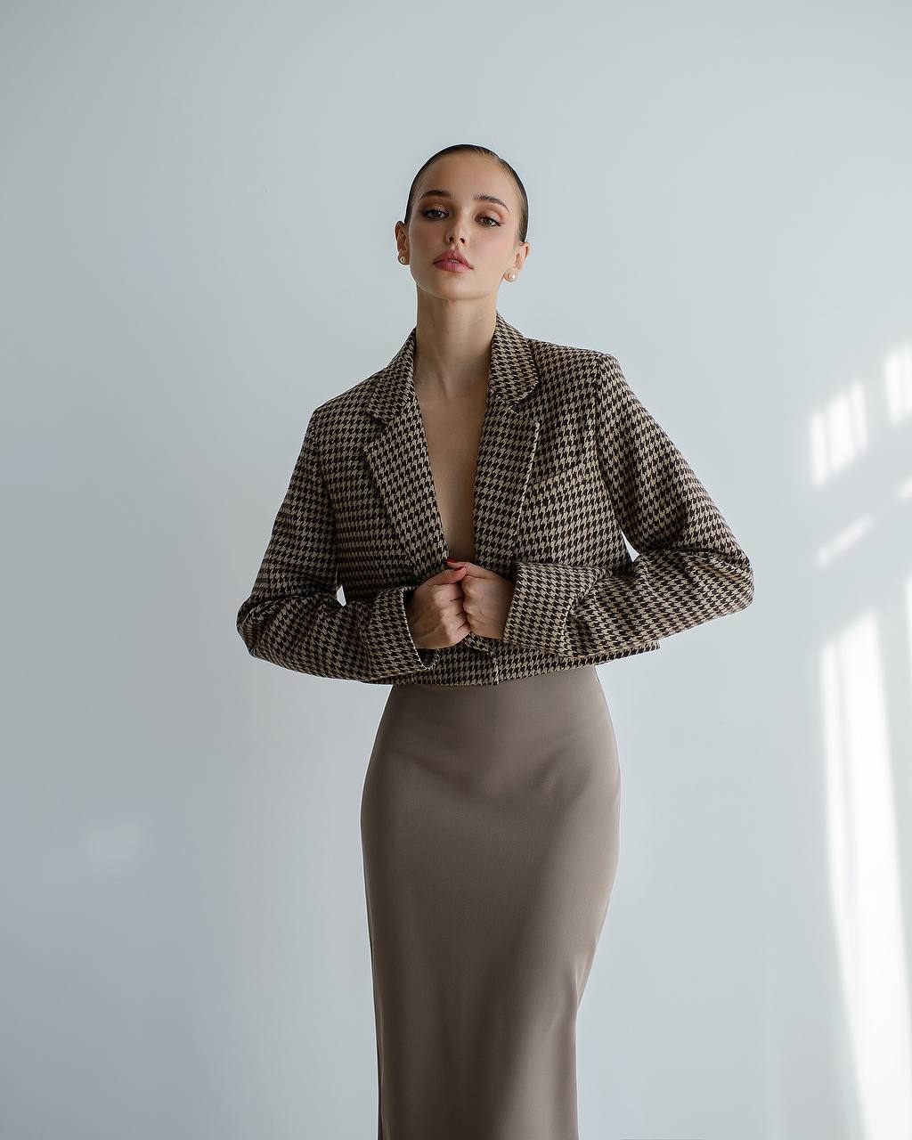 Woman wearing a houndstooth patterned jacket and beige skirt against a light background