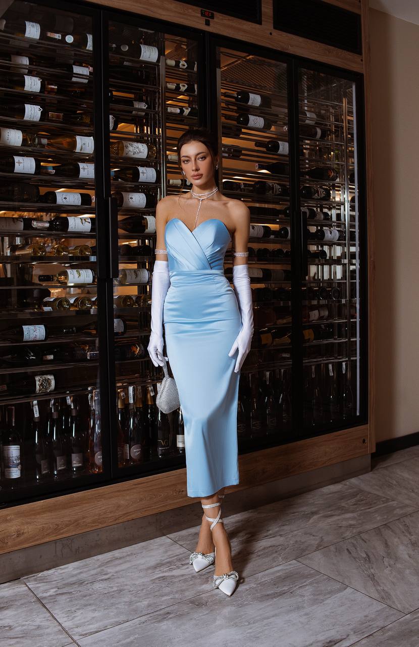 Woman in a light blue dress standing in front of a wine rack.
