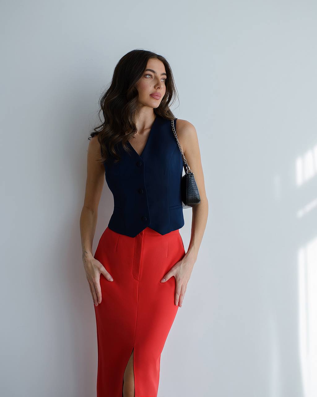 Woman wearing a navy top and red pants against a white wall