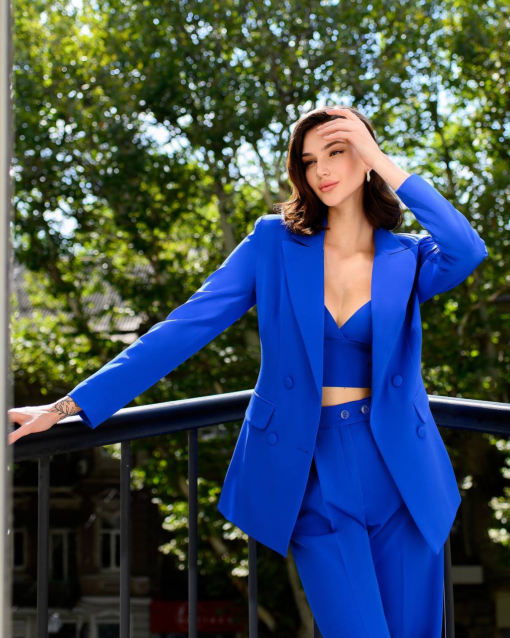 Woman in a blue suit standing on a balcony with trees in the background