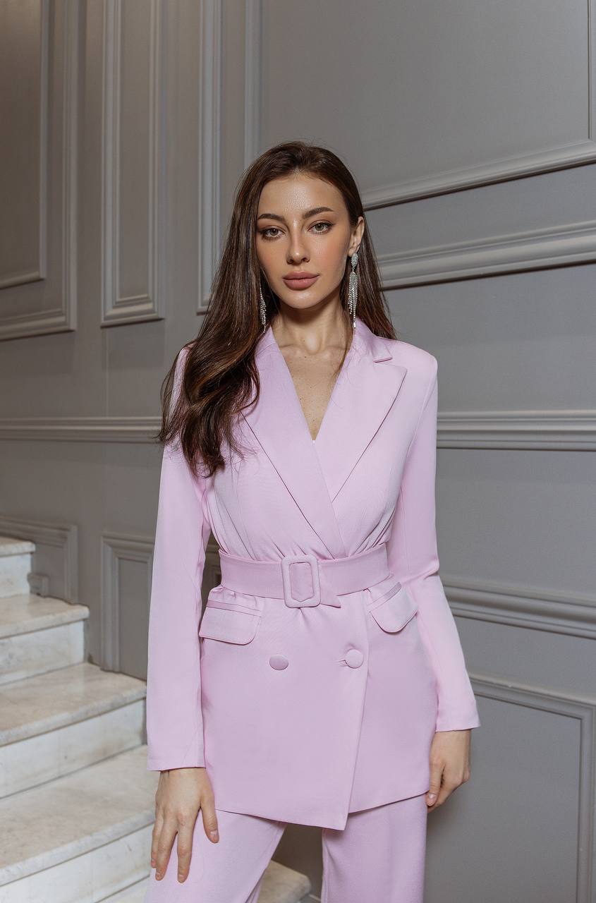 Woman in a pink suit standing in front of a gray paneled wall.