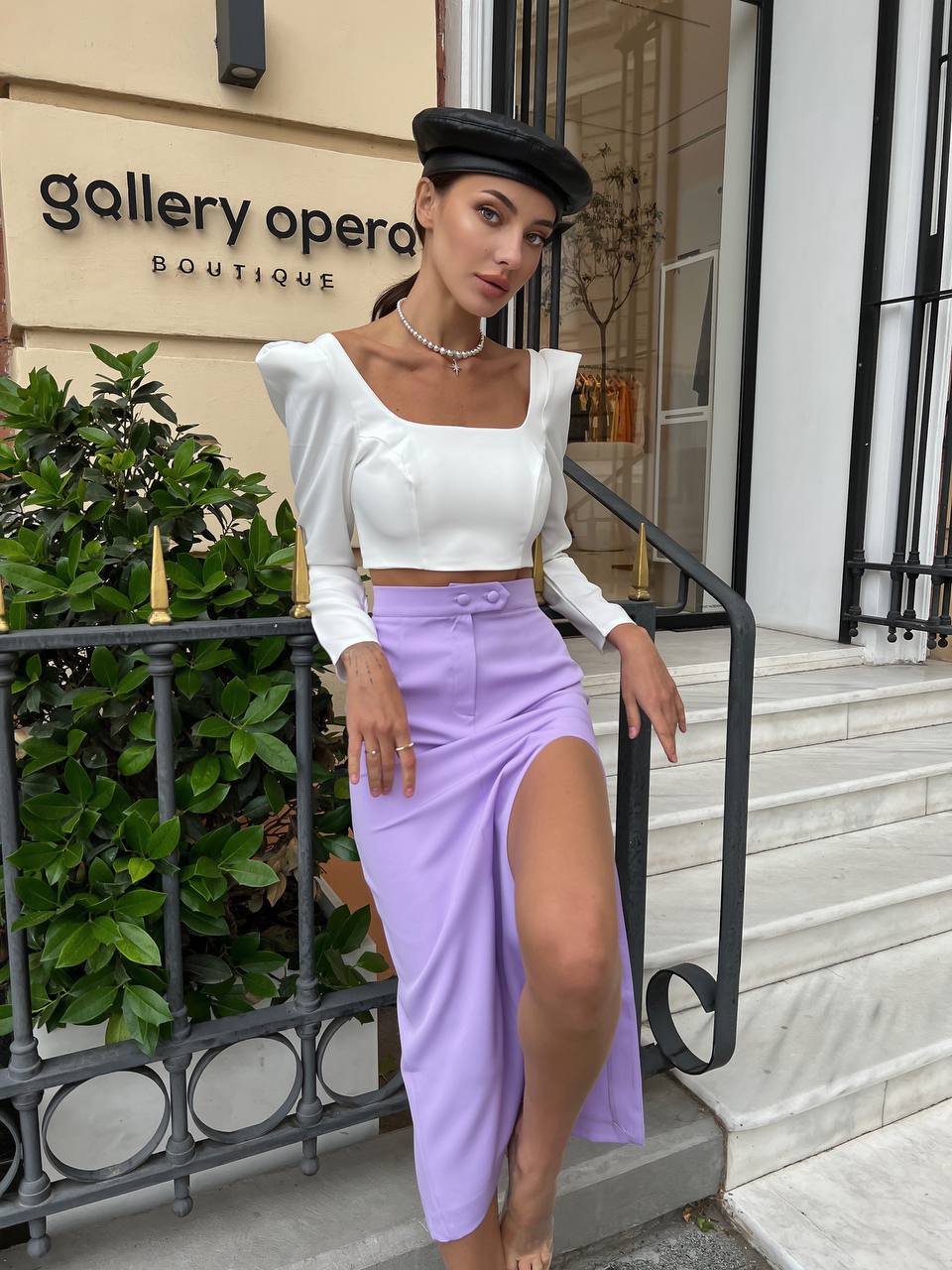 Woman in a white top and purple skirt standing in front of 'Gallery Opera Boutique'.