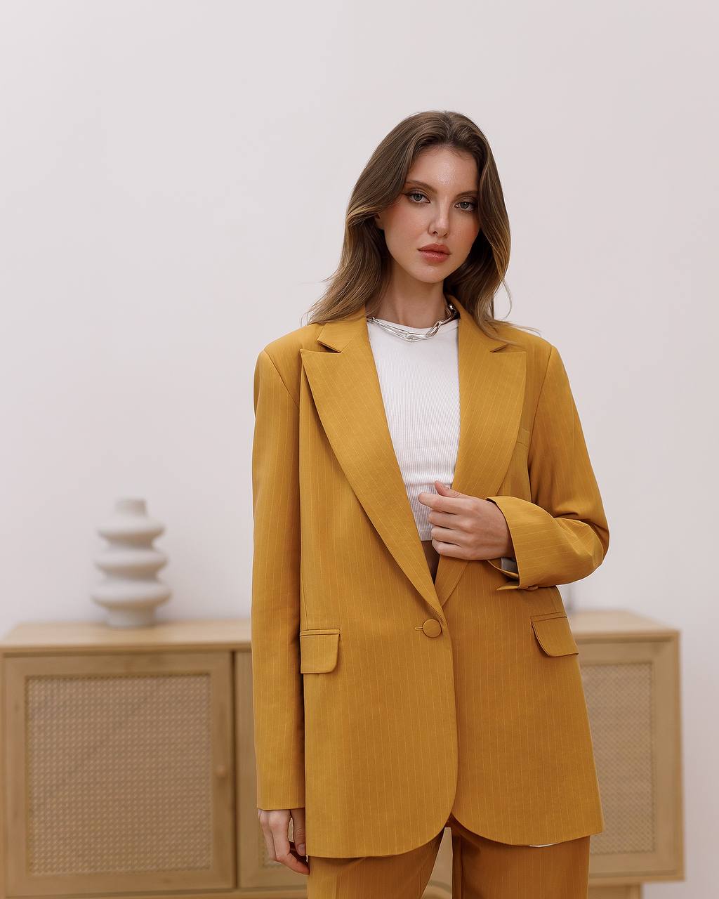 Woman wearing a mustard yellow suit standing in a minimalistic room.