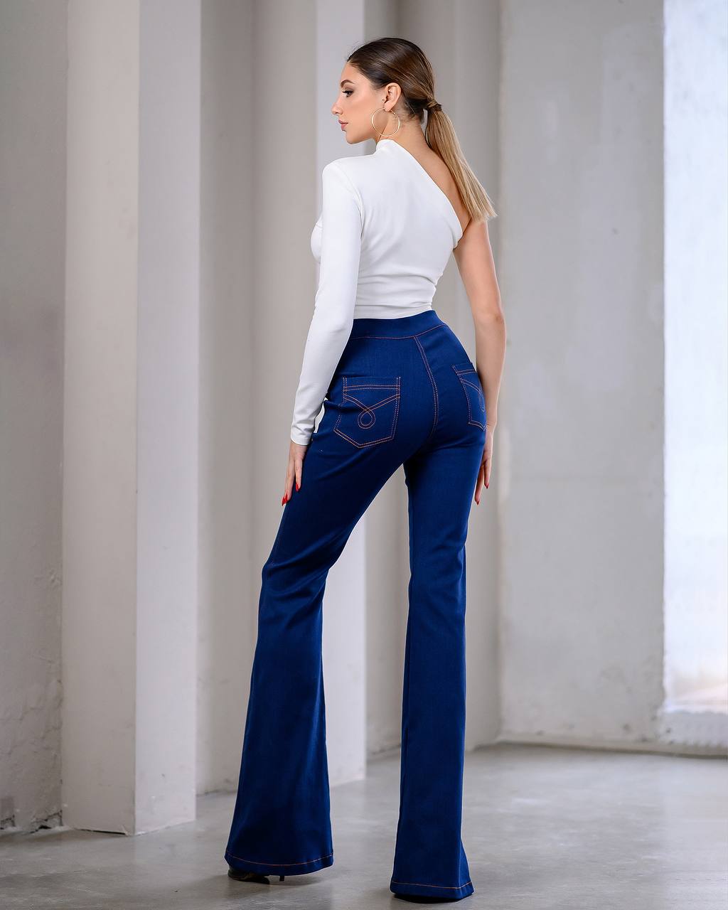 Woman wearing blue flared jeans and a white top in a minimalistic setting