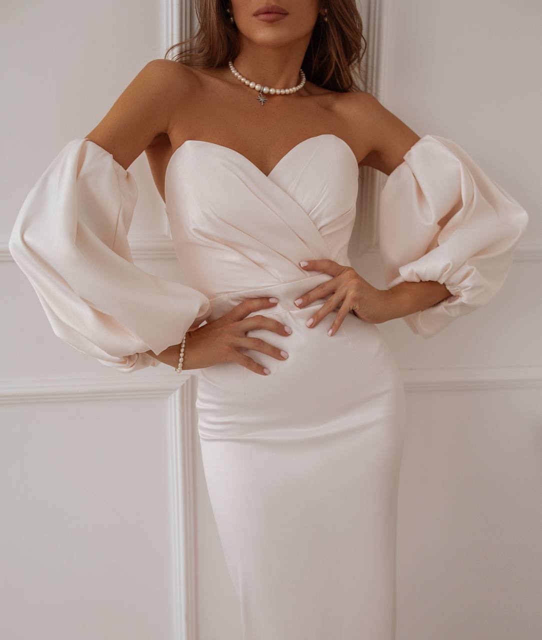 Woman wearing a white off-shoulder dress with puffed sleeves against a plain background