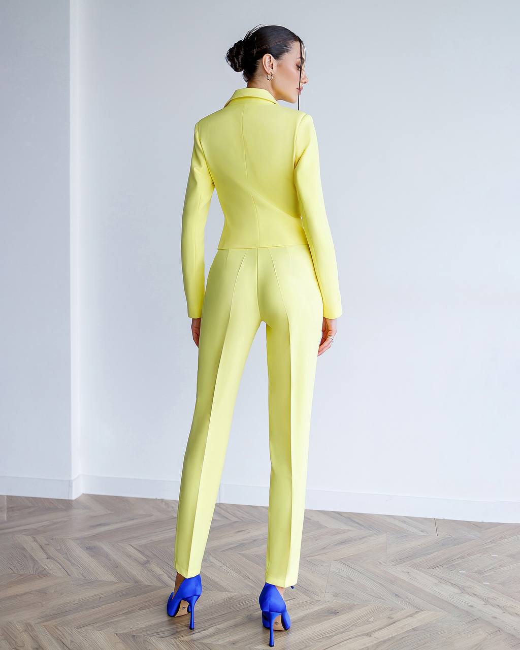 Person wearing a bright yellow suit standing on a wooden floor with a white wall background